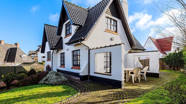 Een traditioneel huis met een steile dakschild, witte buitenmuren en een kleine tuin met een patio tafel en stoelen.