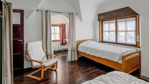 Een slaapkamer met twee enkele bedden, een houten stoel, een radiator en een raam met kantgordijnen.