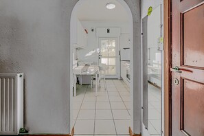 Un couloir étroit, dont le sol est recouvert de carreaux blancs, mène à une pièce où se trouvent une table et une chaise, toutes deux blanches.