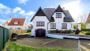 Een huis met twee verdiepingen, voorzien van een zwart dak, witte muren en een bakstenen entree.