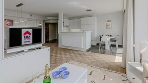 A modern living room with a flat-screen TV, a dining area with a white table and chairs, and a kitchen with white cabinets. - 2 bedroom accommodation in Oostduinkerke (Oostduinkerke)