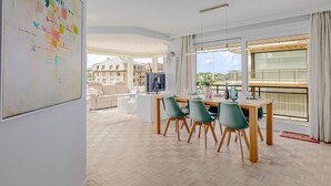 A modern dining area with a wooden table and green chairs, a whiteboard with colorful designs, and large windows offering a view of buildings and greenery. - 2 bedroom accommodation in Oostduinkerke (Oostduinkerke)