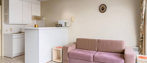 A compact living space with a kitchenette, a sofa, and a small side table.