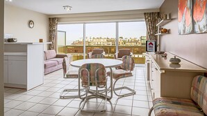 Un salon moderne avec une table à manger ronde, un canapé et une vue sur les immeubles à travers de grandes fenêtres.