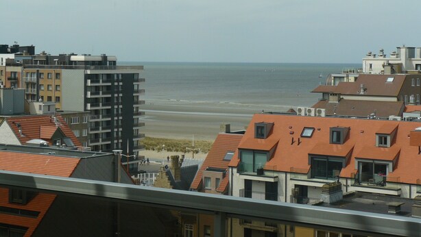 Un paysage urbain côtier avec vue sur la plage, comprenant des bâtiments modernes et traditionnels, dont certains sont dotés de terrasses sur les toits.