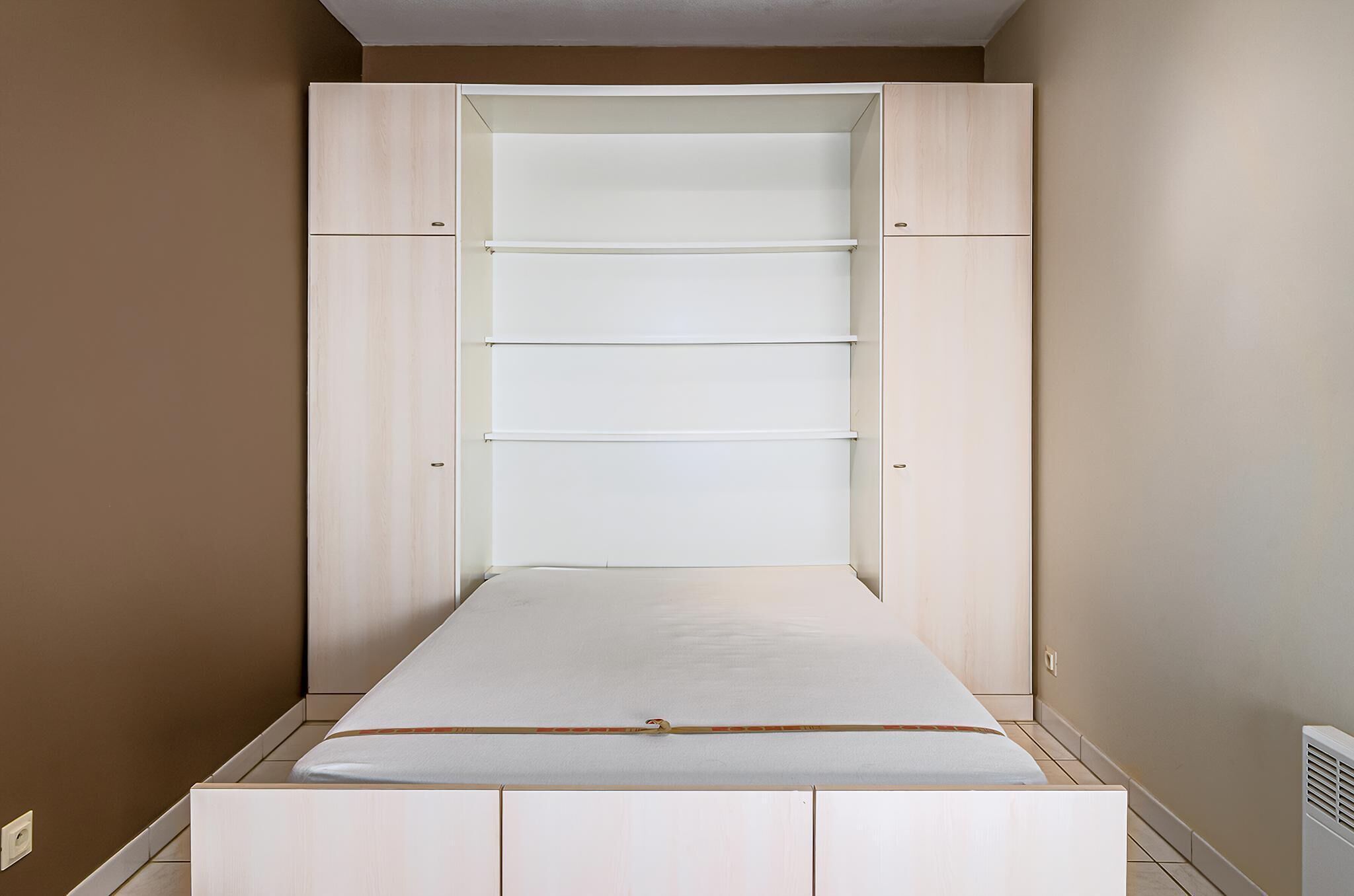 A bedroom with a bed, a wardrobe with multiple shelves, and a radiator.