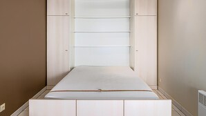 Une chambre à coucher avec un lit, une armoire dotée de plusieurs étagères et un radiateur.