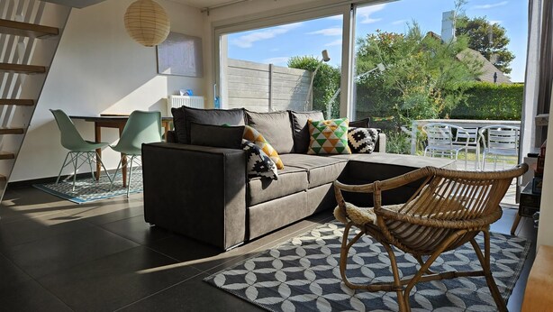 A modern living room with a sofa, chairs, a dining table, and a large window offering a view of the outdoors. - 2 bedroom accommodation in Oostduinkerke (Oostduinkerke)