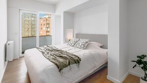 Un dormitorio moderno con una cama grande, una puerta corrediza de vidrio a un balcón y una planta en maceta.