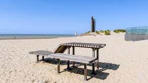 Una playa con un banco de madera y una estatua al fondo.