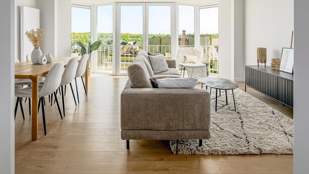 Una sala de estar moderna con un sofá, una mesa de comedor, sillas y vistas al exterior a través de amplios ventanales.