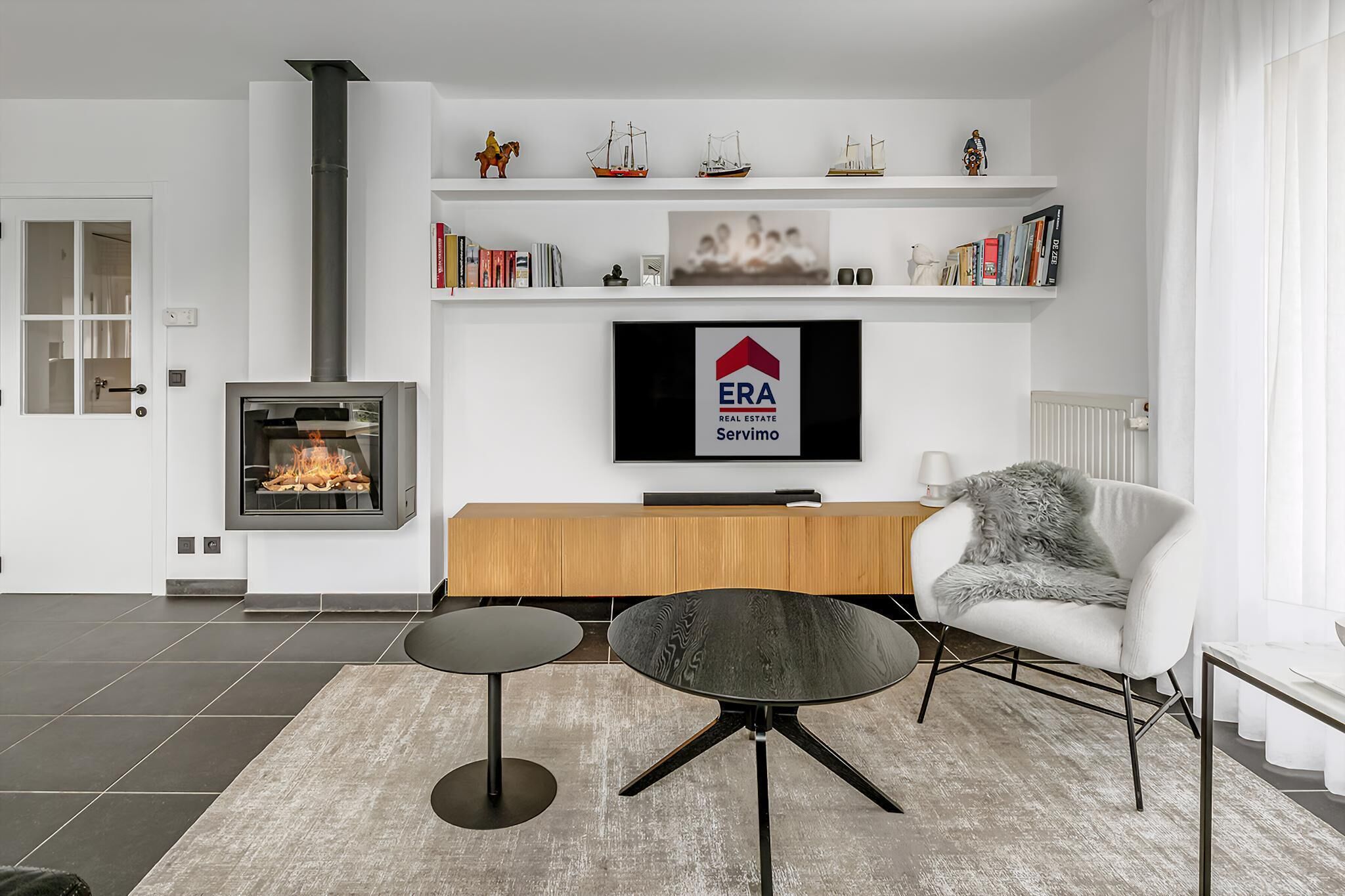 Una sala de estar moderna con chimenea, un televisor montado en la pared y una zona de estar acogedora con un sillón y una mesita.