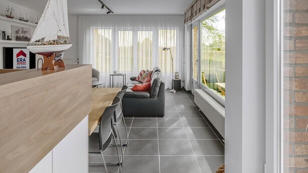 Ein modernes Wohnzimmer mit einem Holzesstisch, einem schwarzen Sofa und einem großen Fenster mit Blick auf Grünflächen.