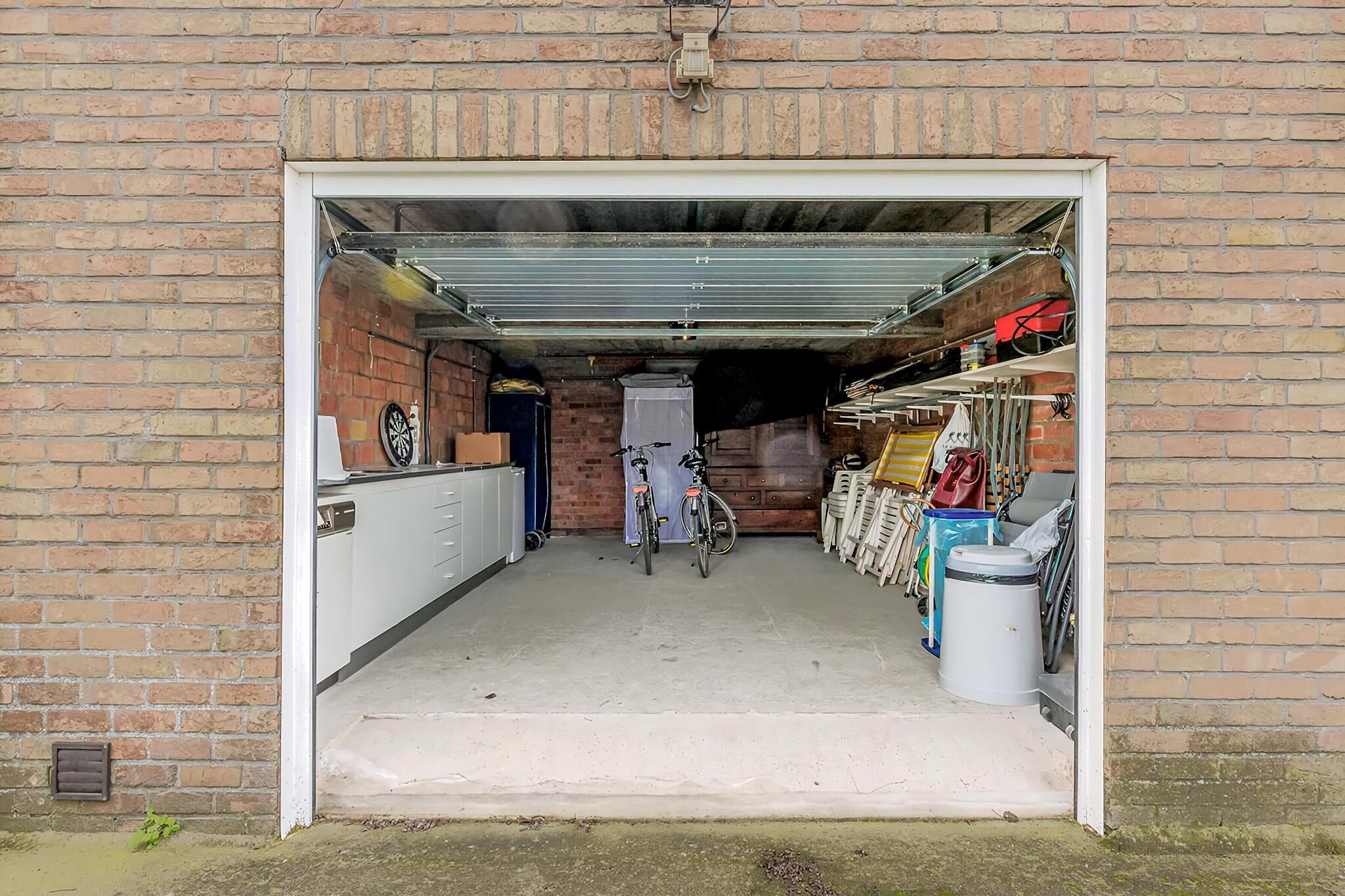 A garage with a bicycle, a trash bin, and a storage area with various items.