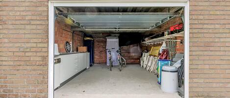 A garage with a bicycle, a trash bin, and a storage area with various items.