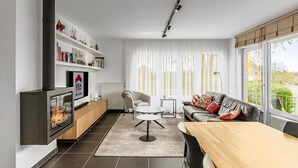 Ein modernes Wohnzimmer mit Kamin, einer Couch, einem Esstisch und Blick ins Freie.