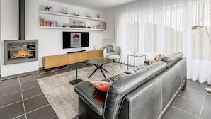 Ein modernes Wohnzimmer mit Kamin, einer Couch, einem Couchtisch und einem an der Wand befestigten Fernseher.