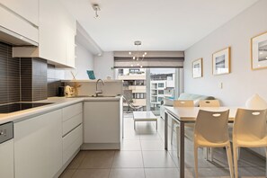 A modern kitchen with white cabinetry, a built-in stove, and a dining area with a table and chairs.