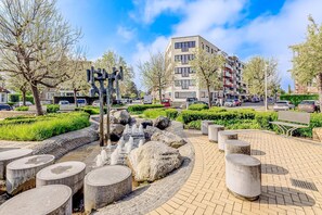 A public park with a fountain, stone benches, and a modern building in the background.