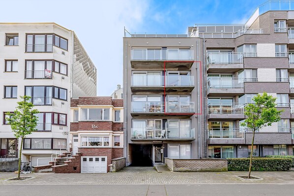 A multi-story residential building with balconies, a garage, and a small entrance area with steps.