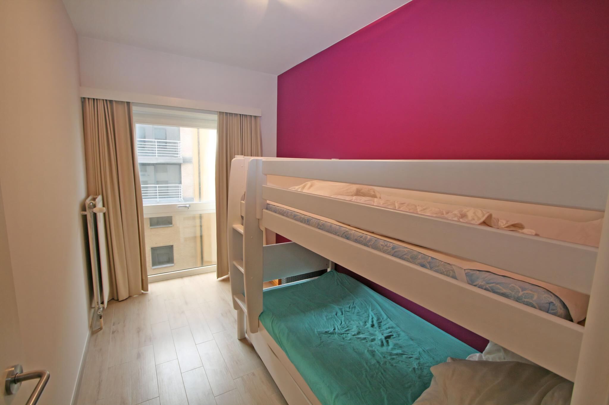Ein Zimmer mit Etagenbett, einem fenster mit Vorhängen und Blick auf ein Gebäude.