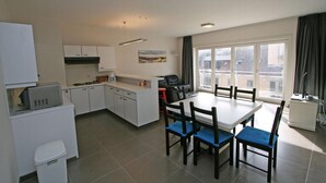 A modern kitchen with white cabinets, a dining table with blue chairs, and a large window offering a view of buildings. - WESTDIEP DOM.0502+G1074 (Nieuwpoort)