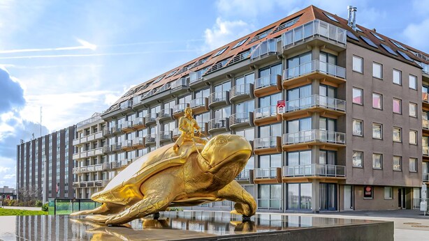 Ein modernes Gebäude mit mehreren Balkonen und einer goldenen Statue einer Figur auf einer Schildkröte.