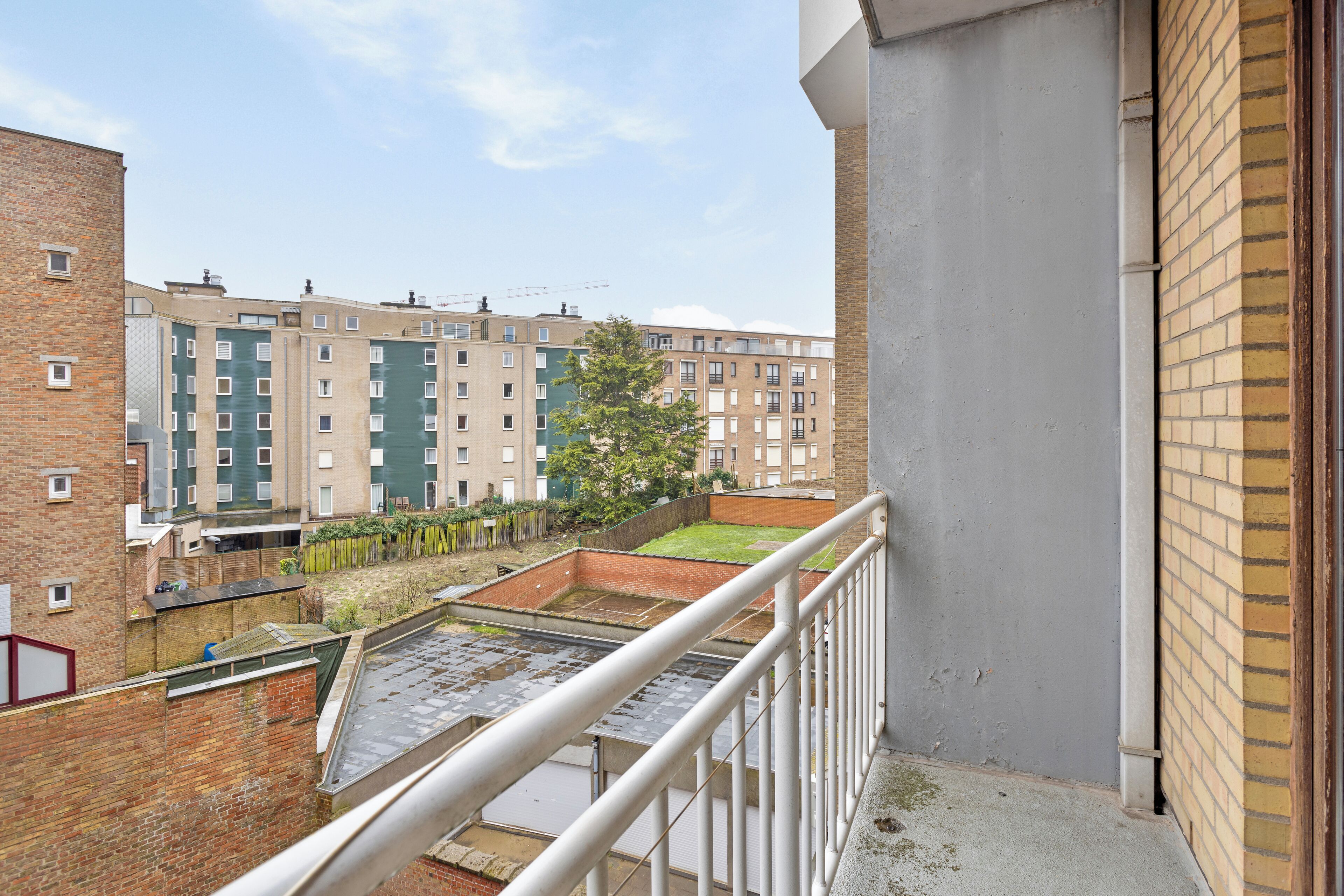 Un edificio residencial con varios pisos, un balcón y un pequeño jardín.