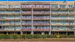 Un hotel de varios pisos con balcones, techo plano y seto delantero.