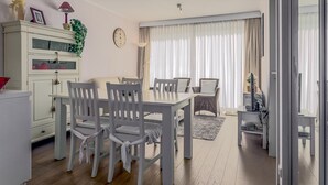 Una sala moderna con comedor, que incluye una mesa de comedor blanca, sillas, un armario blanco y un amplio ventanal con cortinas.