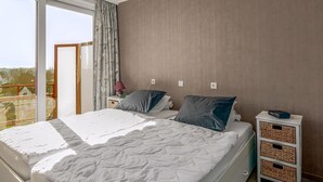Un dormitorio con una cama grande, una mesita de noche, una lámpara y vistas al exterior.
