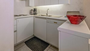Una cocina compacta con armarios blancos, un lavamanos de acero inoxidable, una cafetera y un bol rojo sobre la encimera.