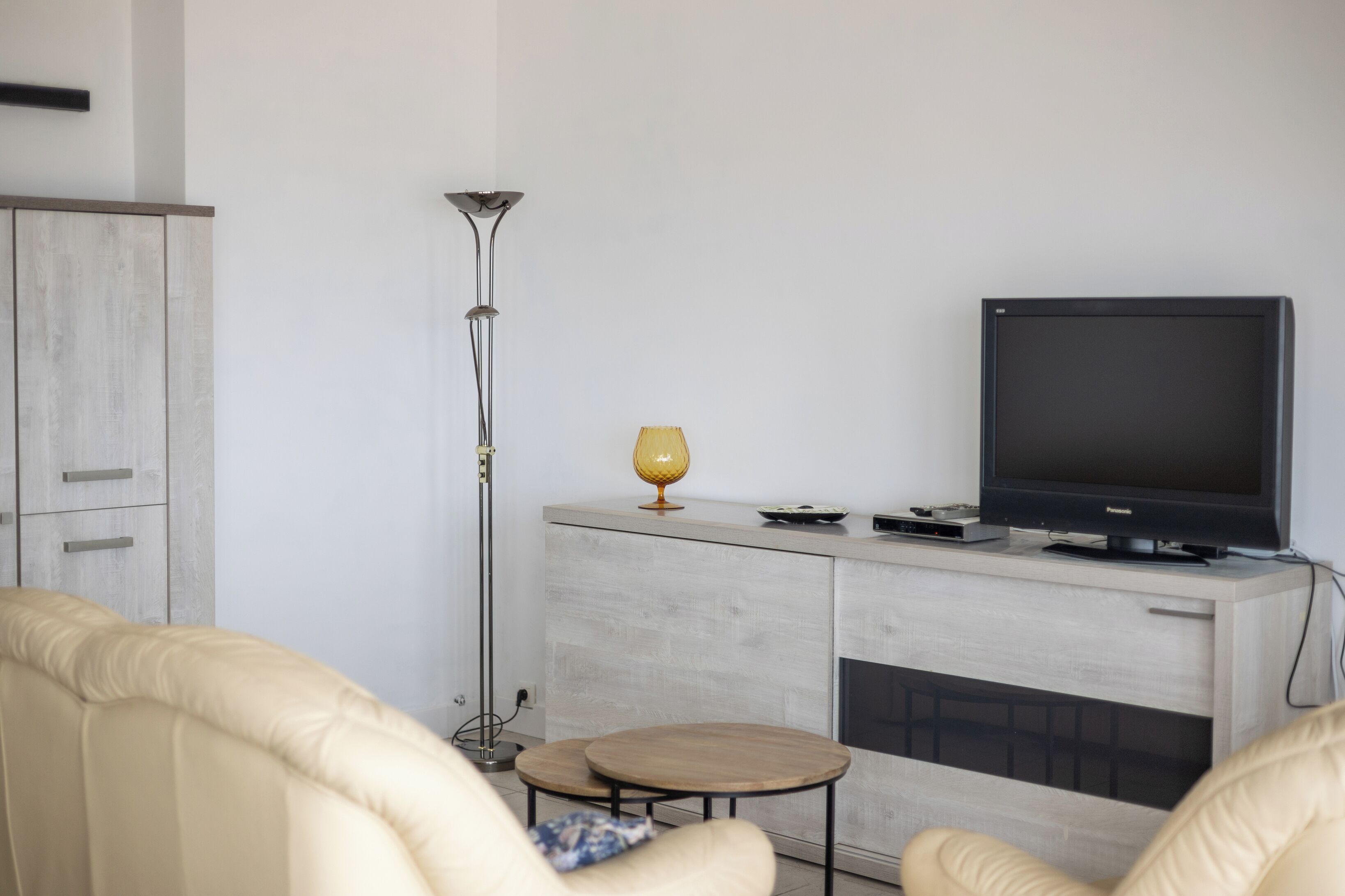 Ein modernes Wohnzimmer mit einer Couch, einem Couchtisch, einem Fernseher auf einer Kommode und einer Stehlampe.