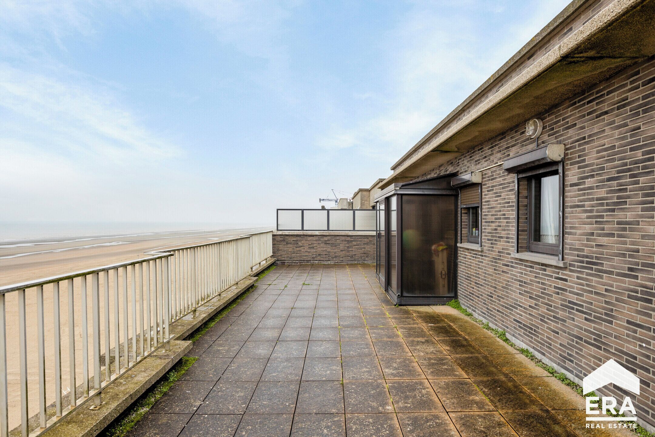 A rooftop terrace with a view of the sea, a brick wall, and a metal railing.