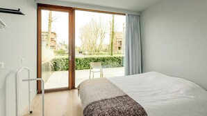 A bedroom with a bed, a chair, a window, and a sliding door to a balcony. - 3 bedroom accommodation in Oostduinkerke (Oostduinkerke)