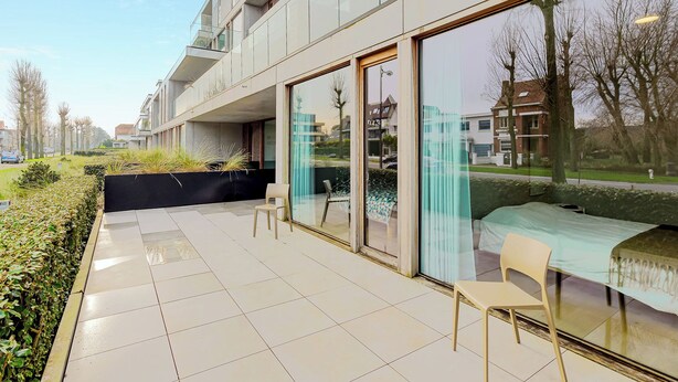 A modern building with large glass windows, a tiled patio area, and outdoor seating. - 3 bedroom accommodation in Oostduinkerke (Oostduinkerke)