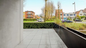 A modern residential area with a paved balcony, a hedge, and a view of neighboring houses and parked cars. - 3 bedroom accommodation in Oostduinkerke (Oostduinkerke)