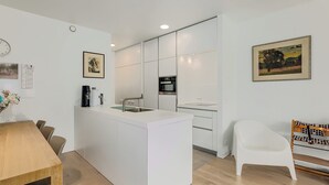 A modern kitchen with a central island, white cabinetry, and a dining area with a wooden table and chairs. - 3 bedroom accommodation in Oostduinkerke (Oostduinkerke)