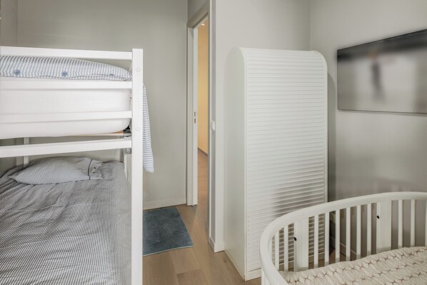 A bedroom with a bunk bed, a wardrobe, a crib, and a large mirror on the wall.