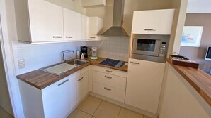 A compact kitchen with white cabinets, a stainless steel sink, a built-in oven, and a microwave. - 2 bedroom accommodation in Nieuwpoort (Nieuwpoort)