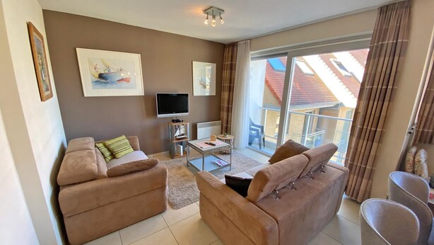 A modern living room with two sofas, a flat-screen TV, a small table, and a balcony with a view of buildings. - 2 bedroom accommodation in Nieuwpoort (Nieuwpoort)