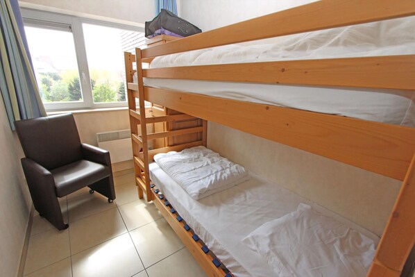 A bunk bed with a chair and a window in a room.
