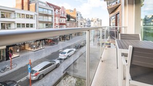 A modern building with a glass balcony overlooking a street with cars and shops.