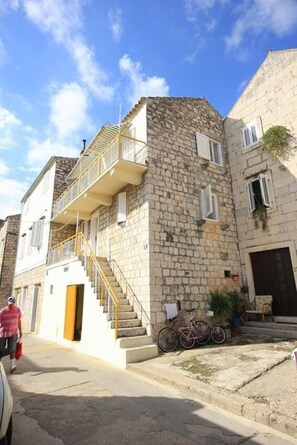Un bâtiment en pierre de deux étages, doté d’un balcon, d’un escalier et d’un vélo garé à l’extérieur.