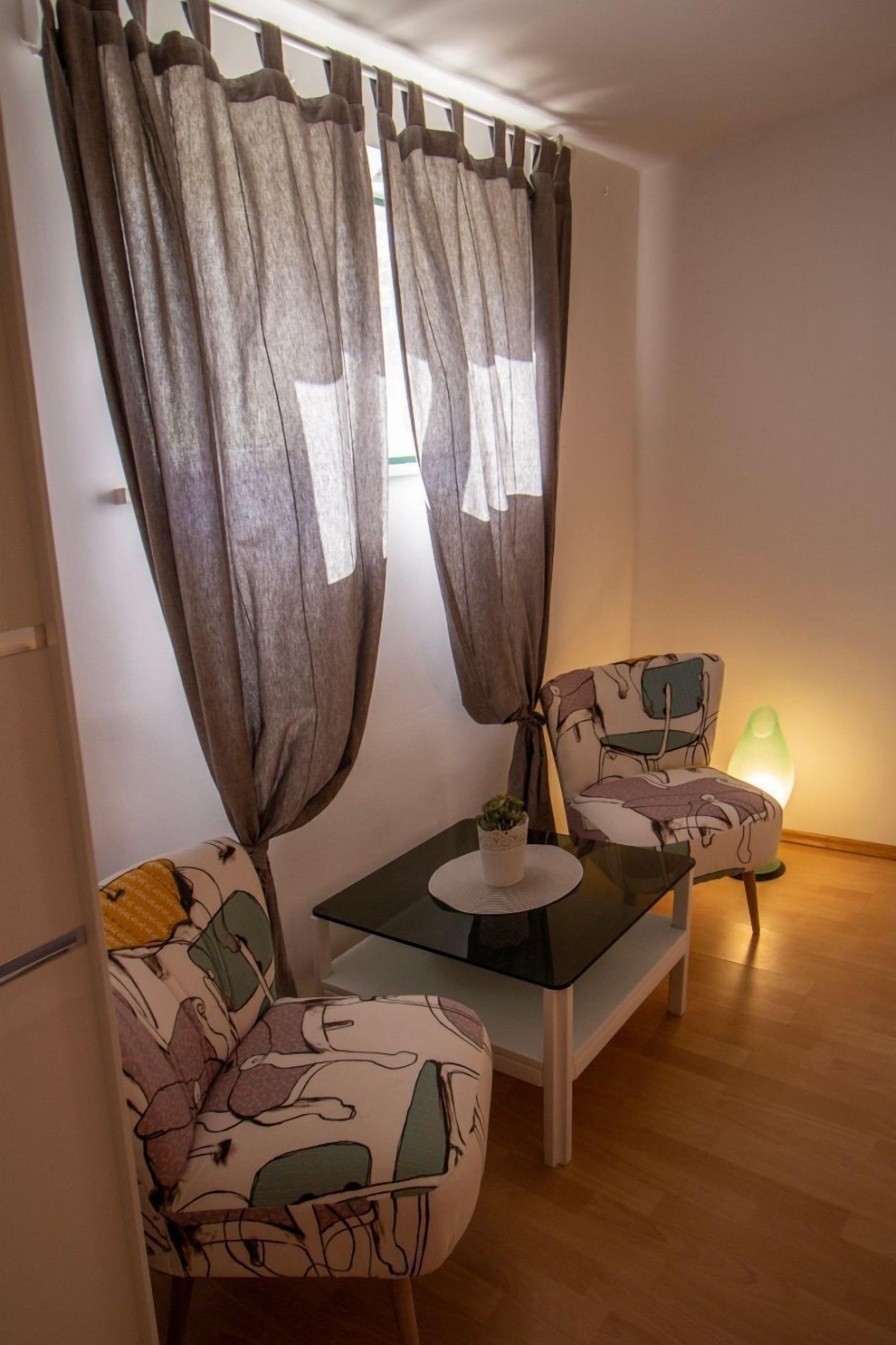 A small, cozy room with a table and two chairs, a potted plant, and a green lamp.