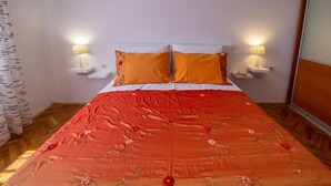 A bed with a red floral bedspread, two white nightstands with lamps, and a wooden floor. - Apartment Zvone (Supetar)
