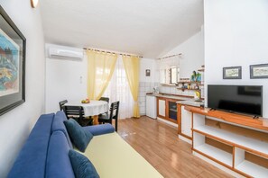 Ein kompakter Wohnbereich mit Sofa, Esstisch, Stühlen, einer Küchenzeile und einem Fernseher.