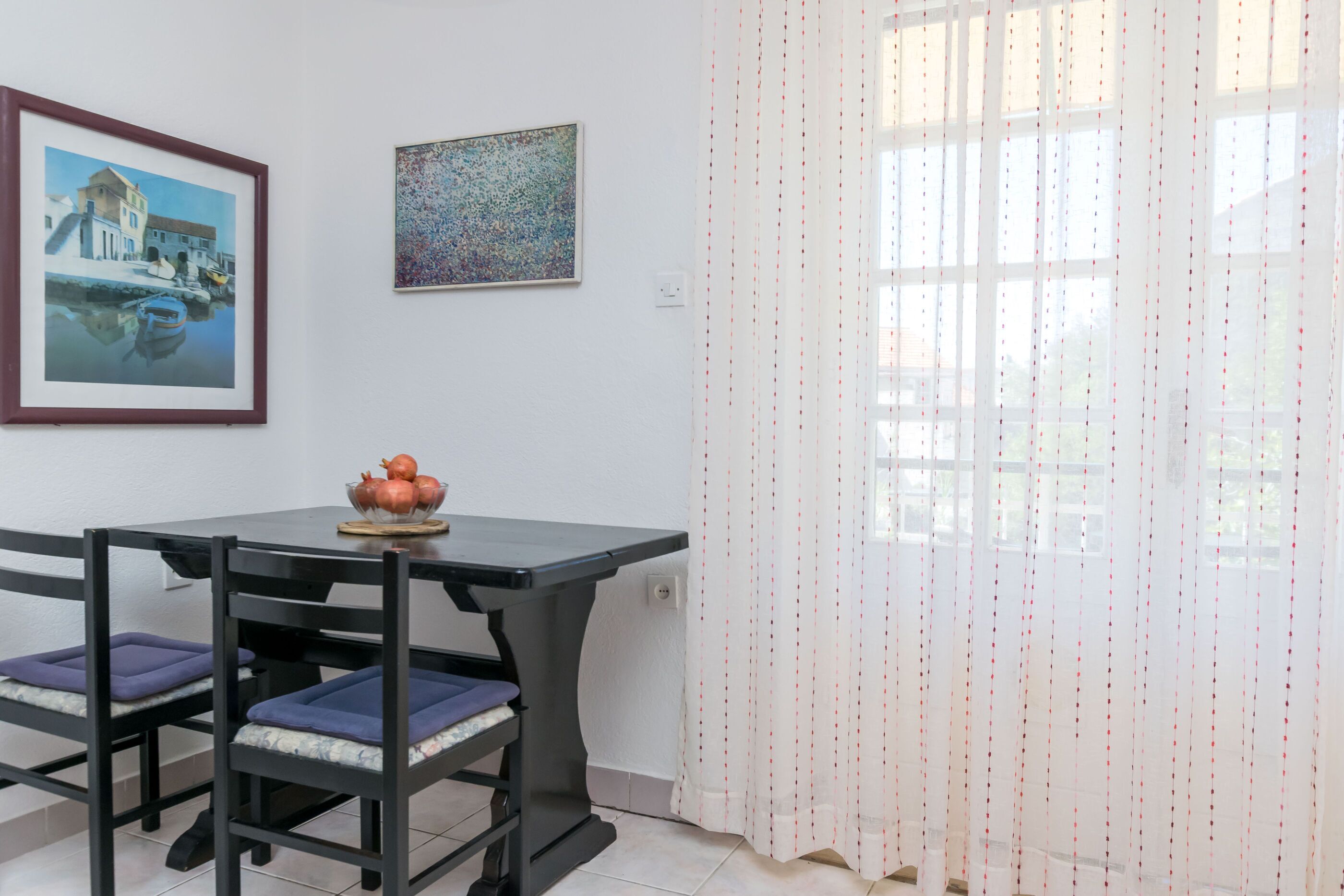A dining area with a table and chairs, a framed painting, and a decorative curtain.