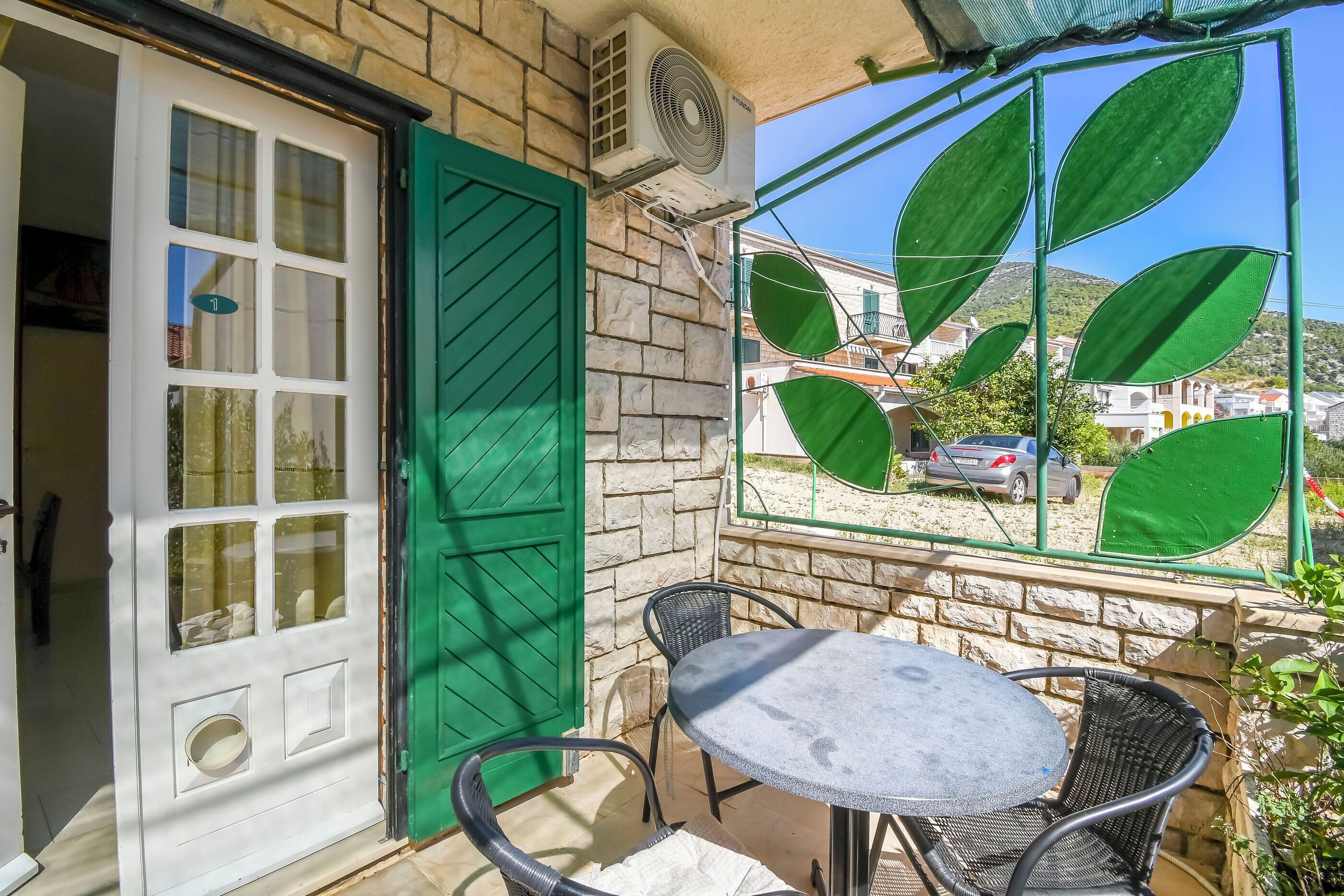 A patio with a table and chairs, a green door, and a window with green leaf-shaped blinds.