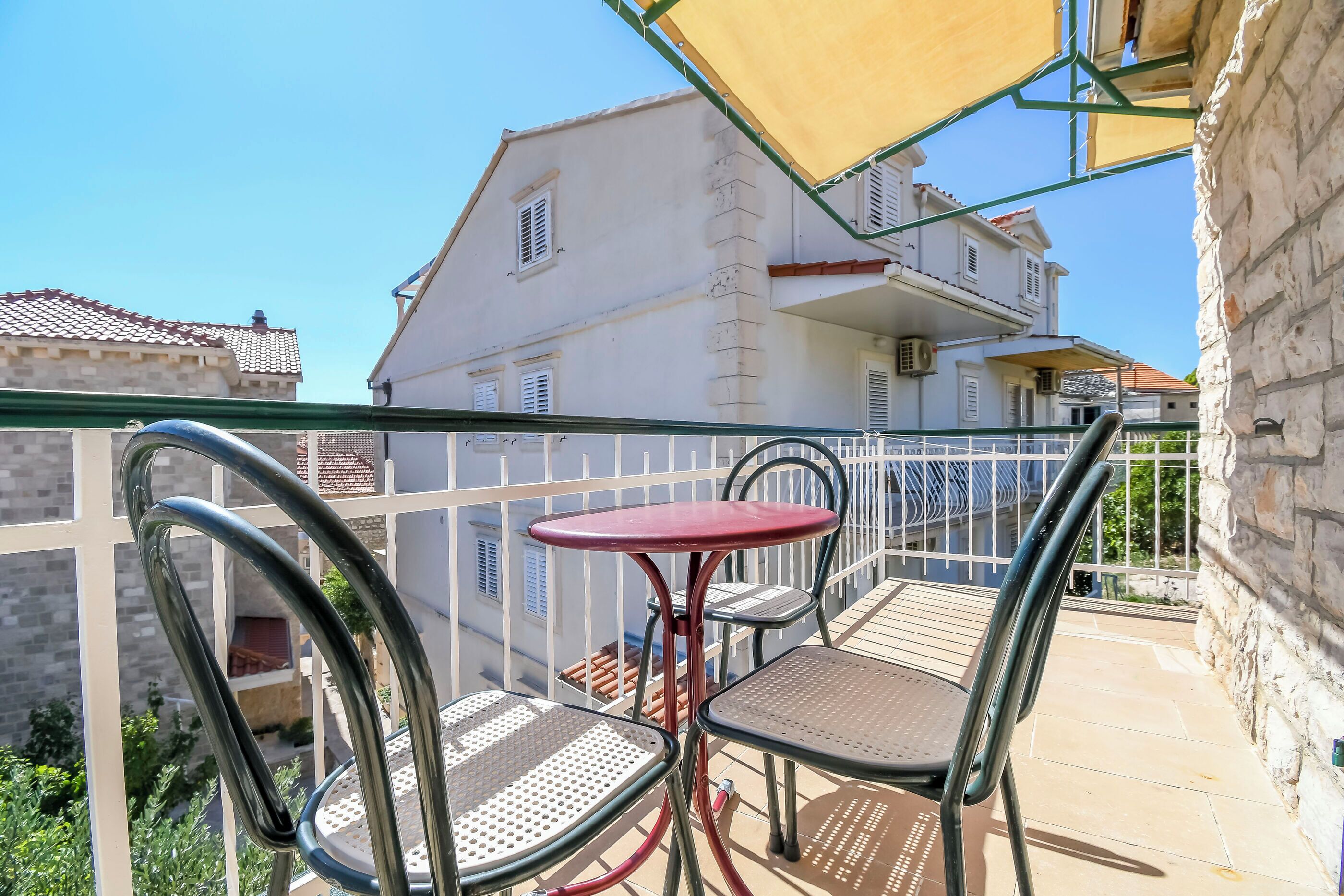 A balcony with a metal table and chairs, a yellow umbrella, and a view of a white building with balconies.